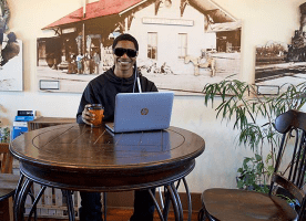 A blind man smiles in a coffee shop while he listens to NFB-NEWSLINE on his laptop.
