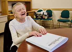 A smiling senior woman reads a Braille book